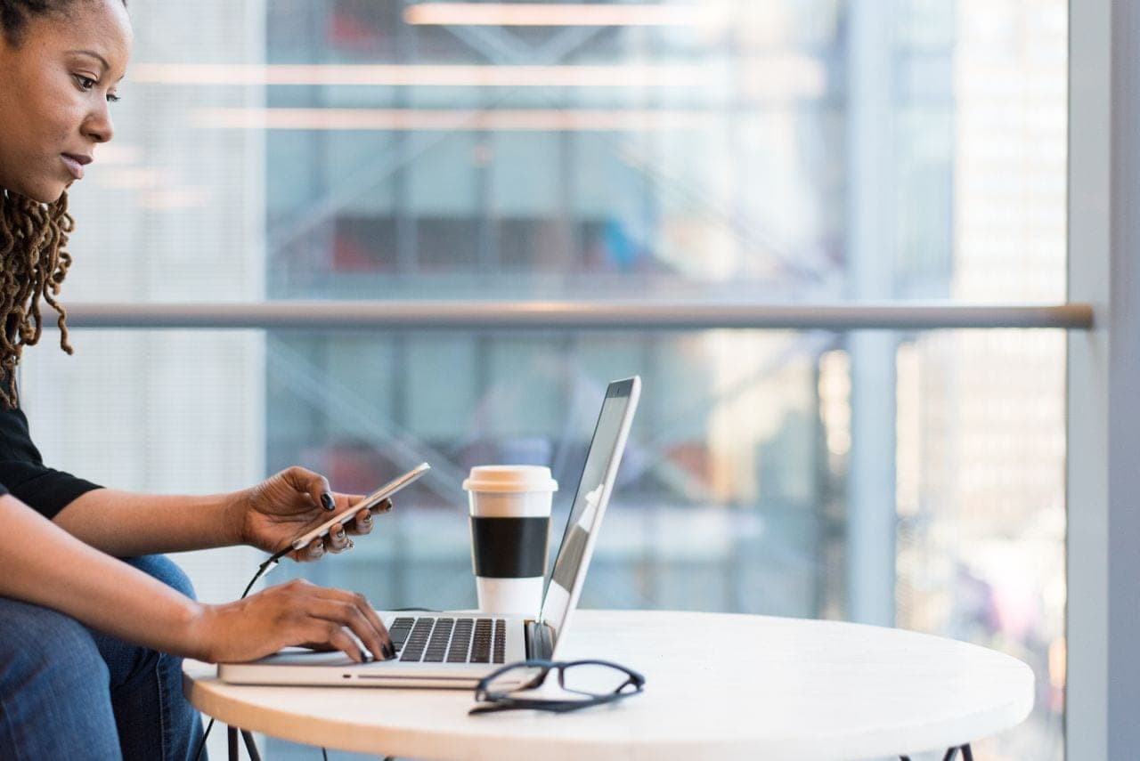 A woman works on a laptop at a café table with a coffee cup