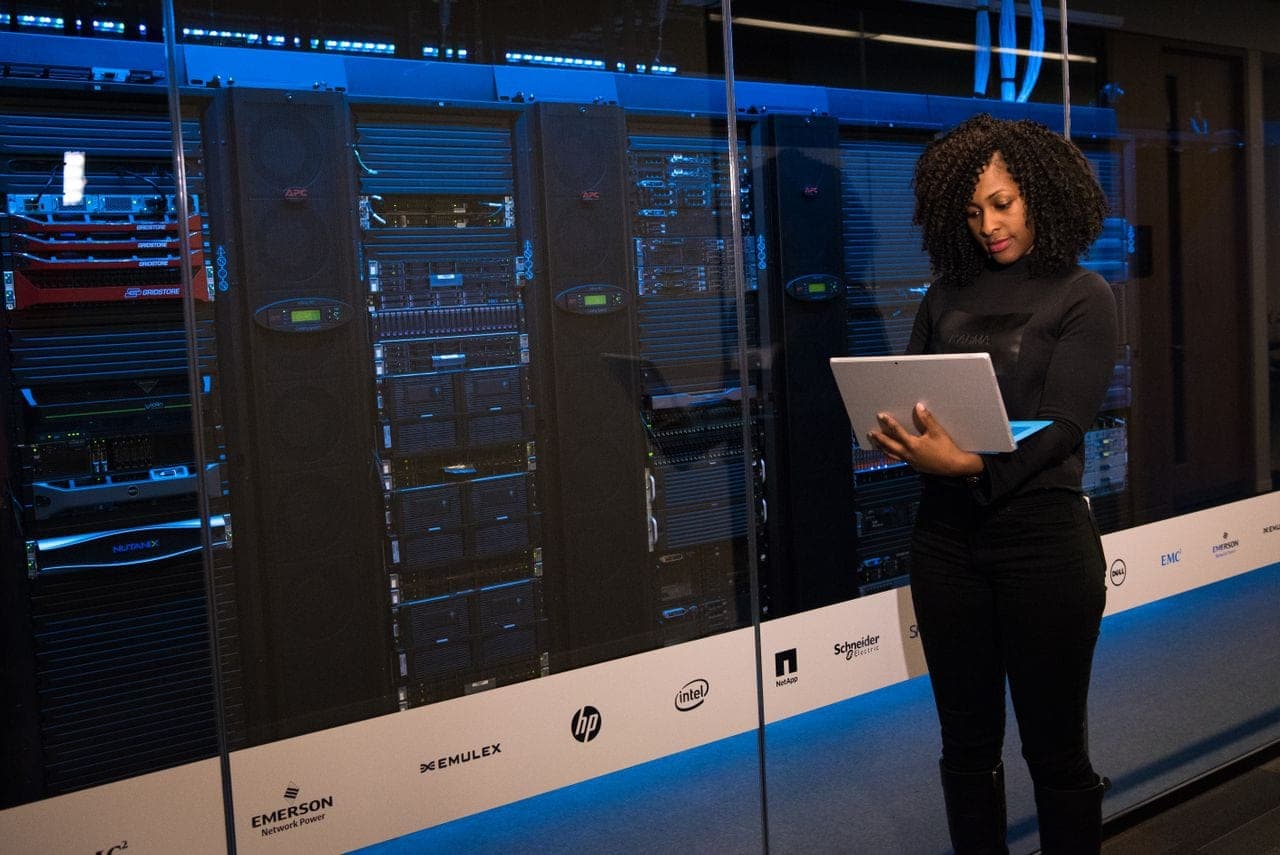 An engineer with a laptop stands beside server racks in a data centre