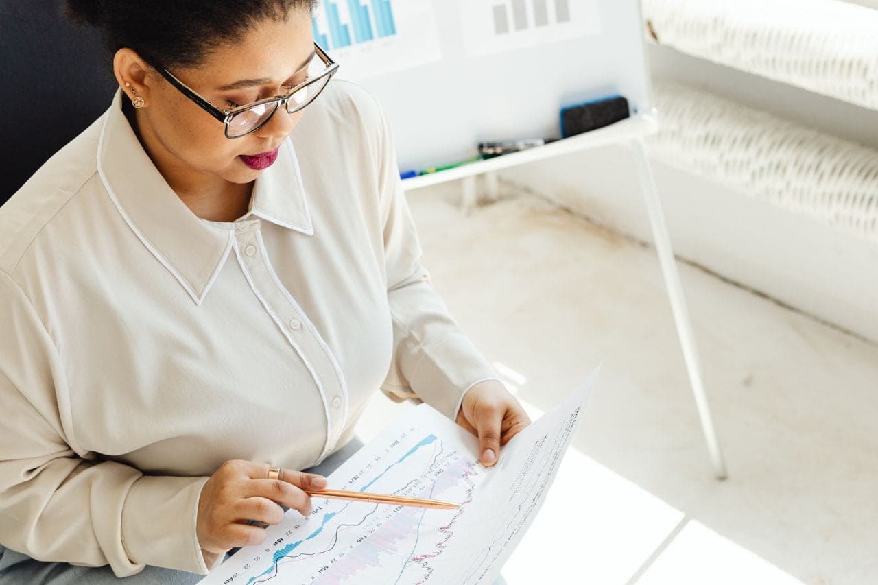 A woman in glasses reviews printed charts at a white desk
