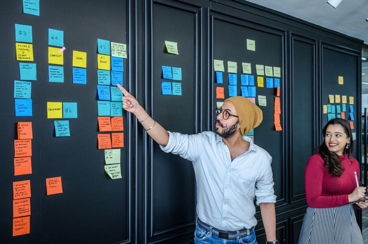 Two colleagues plan with sticky notes on a dark wall board
