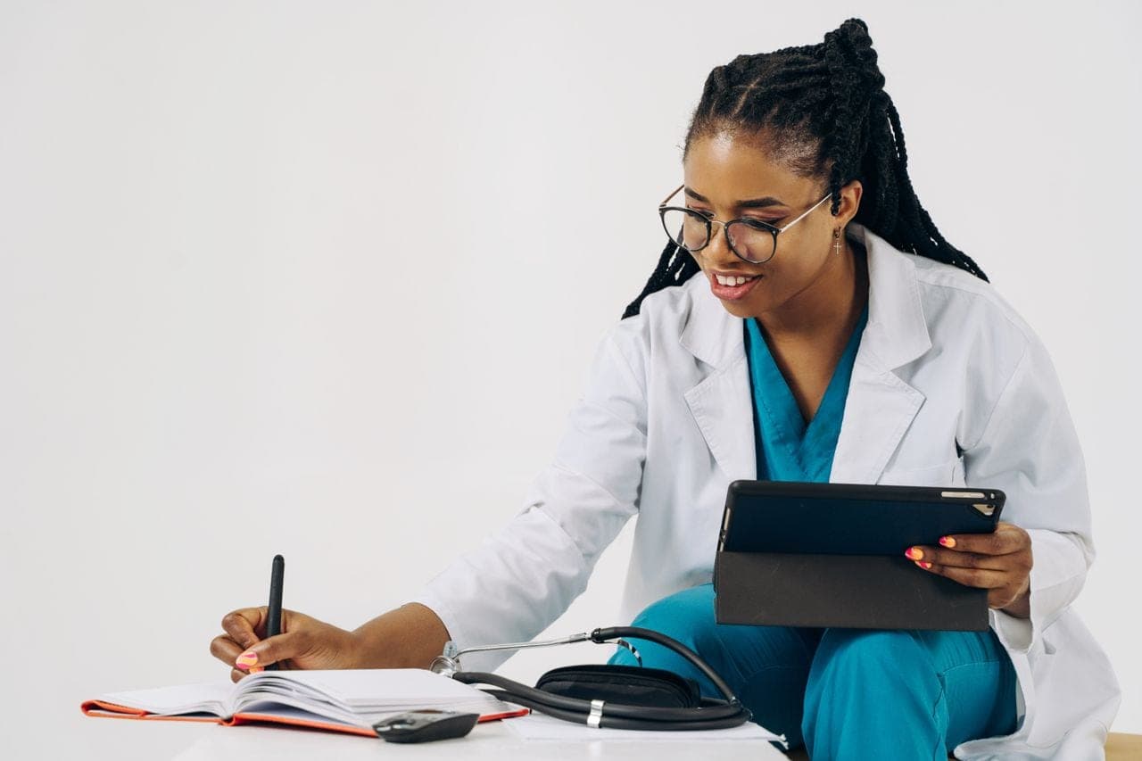 A doctor in a white coat writes notes while holding a tablet