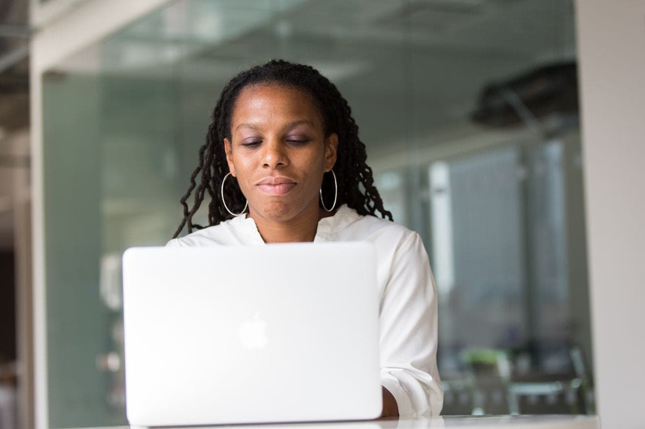 A woman with braids works on a laptop in a glass-walled office
