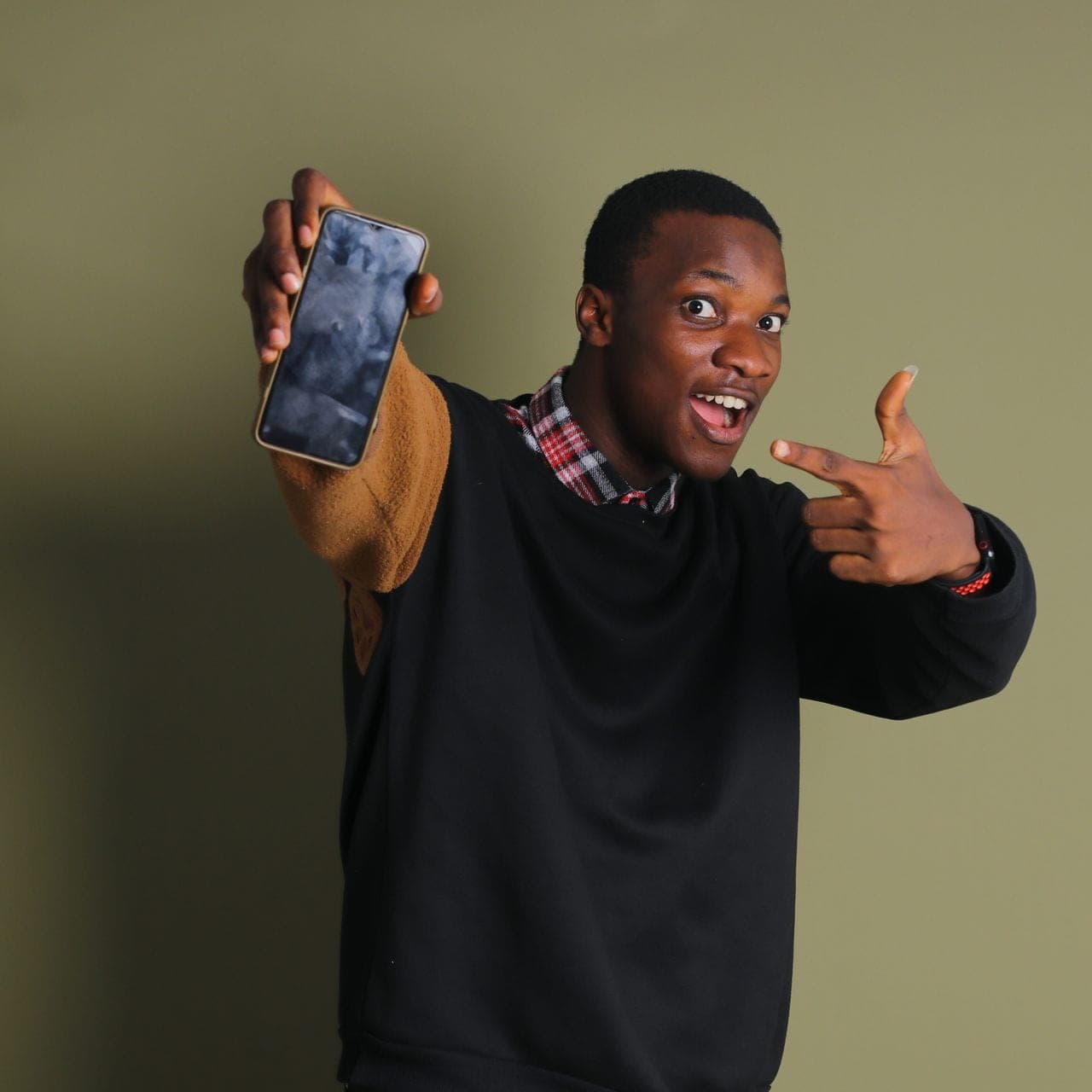 A young man smiles and points at the smartphone he is holding