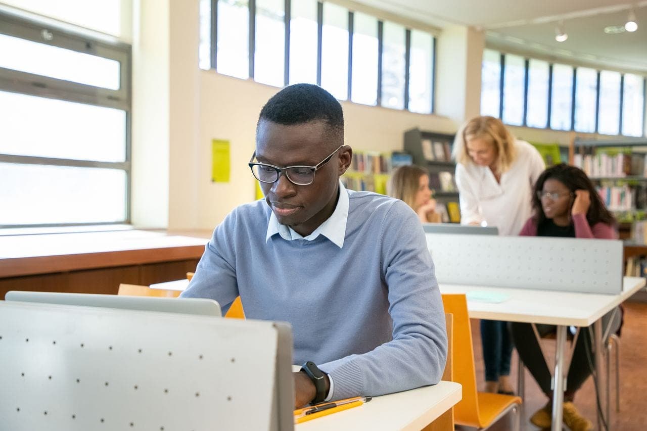 A man in a blue jumper works on a laptop in a bright open office