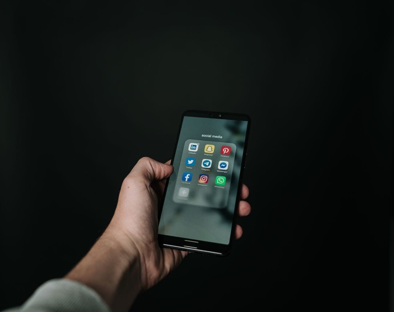 A hand holds a smartphone showing app icons against a dark background